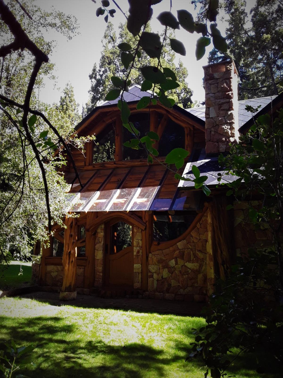 fachada rústica de pedra e madeira em floresta — projeto Cabaña en San Carlos de Bariloche, por ESTUDIO ARQ.GABRIEL ARIAS, em San Carlos de Bariloche